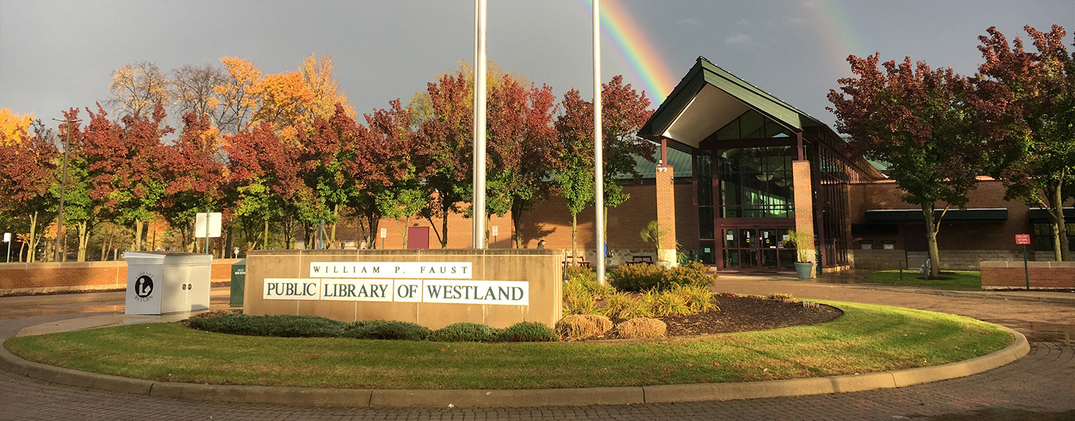 Image of the entrance of a building. The building entrance has a steepled green roof. In front of the building, a sign reads, "William P. Faust Public Library of Westland". There's a rainbow in the sky.